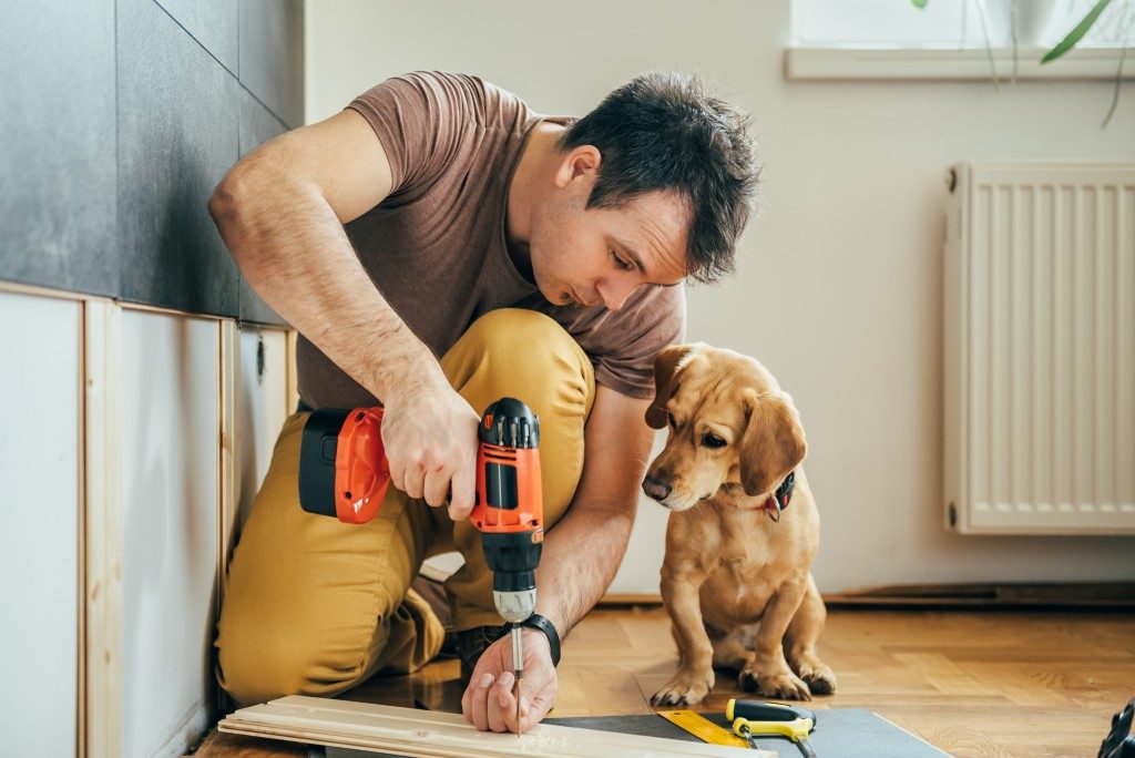 man constructing something in house while dog watches