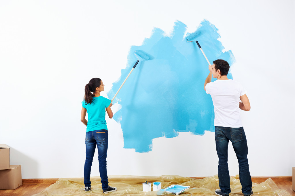 Young couple brushing the wall of their new home with sky blue color
