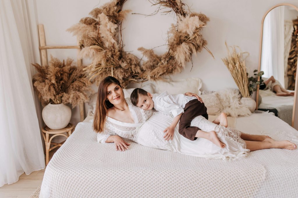 pregnant woman lying down on a bed with his son, with rustic maternity shoot props in the background