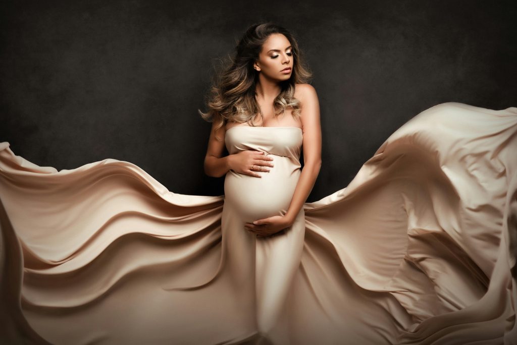 pregnant woman in a beige flowy dress, posing for an at home maternity shoot