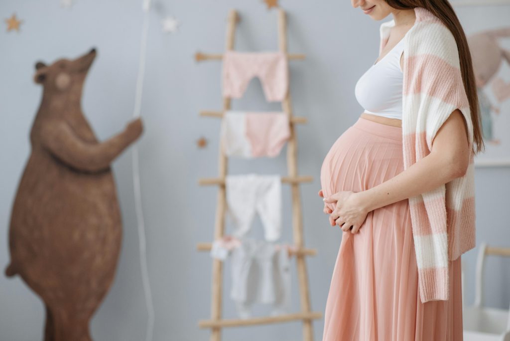 pregnant woman in a pink dress holding her baby bump, with wall props in the background